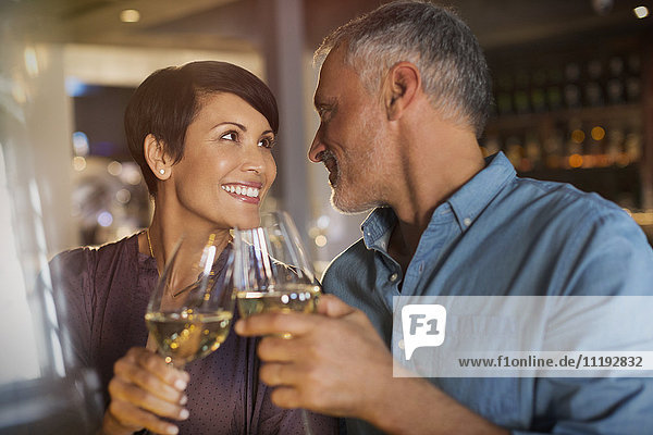 Couple toasting white wine glasses in restaurant