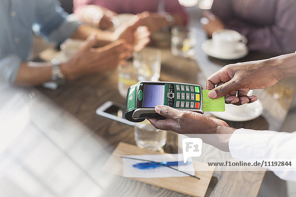 Kellner mit Kreditkartenlesegerät am Restauranttisch