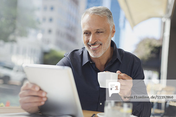 Smiling businessman using digital tablet drinking coffee at urban sidewalk cafe