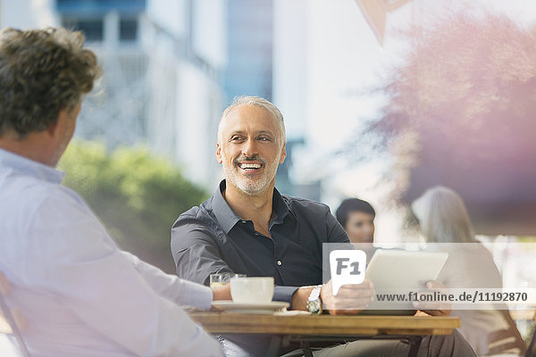 Lächelnde Geschäftsleute  die sich unterhalten  Kaffee trinken und ein digitales Tablet in einem Straßencafé benutzen