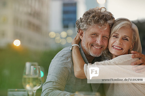 Portrait smiling senior couple hugging at urban sidewalk cafe