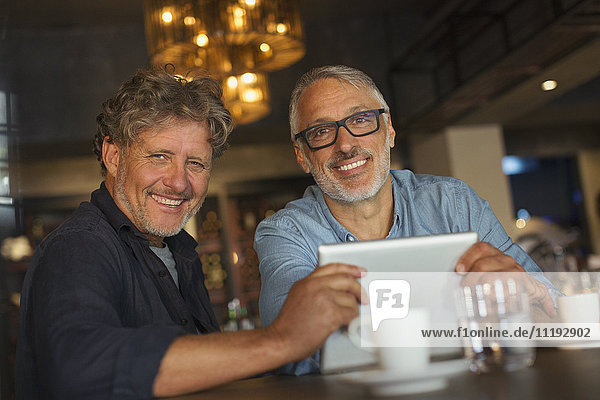 Porträt eines lächelnden Mannes  der ein digitales Tablet benutzt und am Restauranttisch Kaffee trinkt