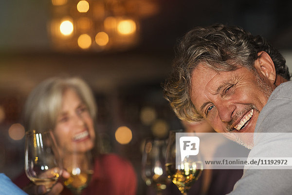 Portrait laughing senior man drinking white wine with friends at bar