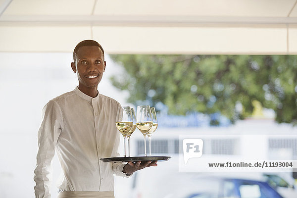 Portrait smiling waiter serving white wine on tray in restaurant