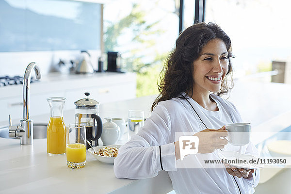 Smiling woman in bathrobe drinking coffee in morning kitchen