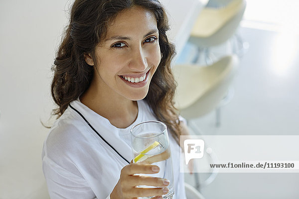 Porträt einer lächelnden Frau im Bademantel  die Wasser mit Zitrone trinkt