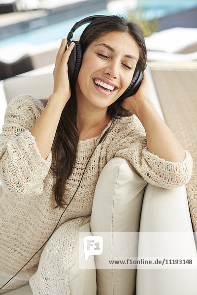 Unbeschwerte Frau  die auf dem Sofa mit Kopfhörern Musik hört
