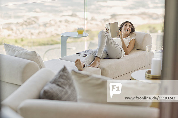 Lächelnde Frau liest ein Buch und entspannt sich auf einem Liegestuhl