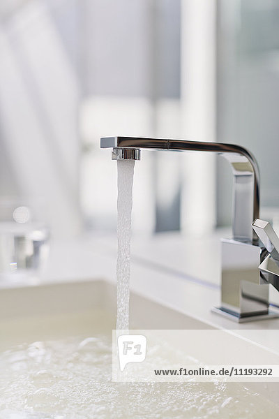 Water from modern faucet filling bathroom sink