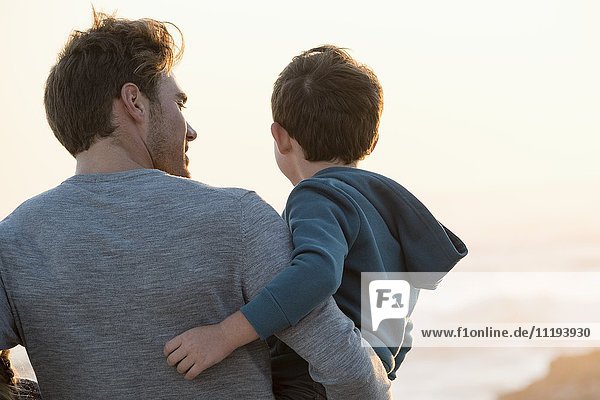 Glücklicher Vater und Sohn stehen bei Sonnenuntergang am Strand.