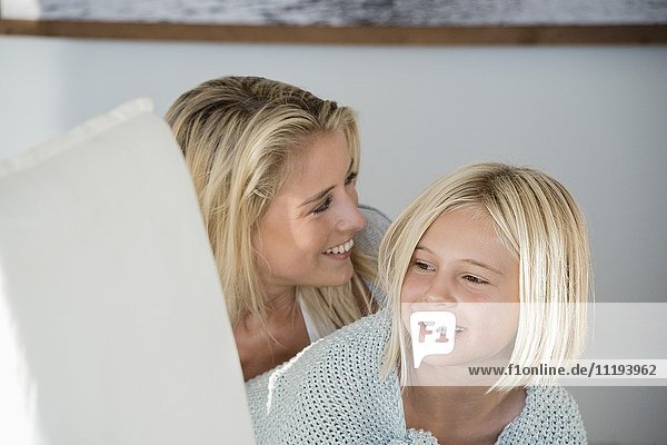 Glückliche Mutter und Tochter lächelnd im Wohnzimmer