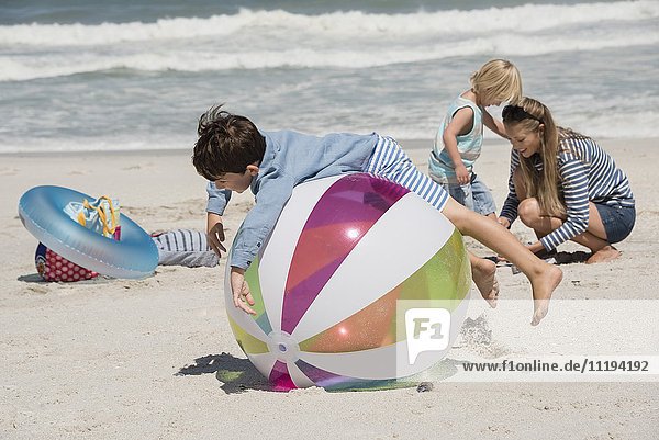 Frau mit ihren beiden Kindern beim Spielen am Strand