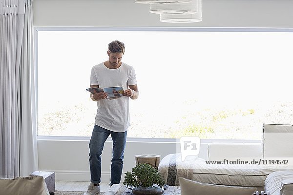 Junger Mann beim Lesen einer Zeitschrift im Wohnzimmer zu Hause