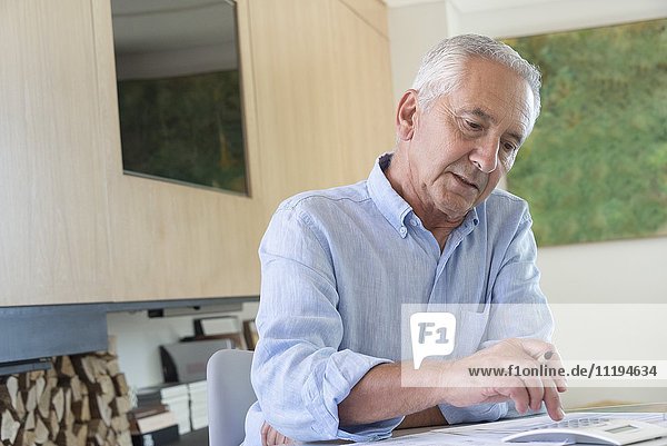 Älterer Mann  der einen Taschenrechner benutzt  während er zu Hause Papierkram erledigt.