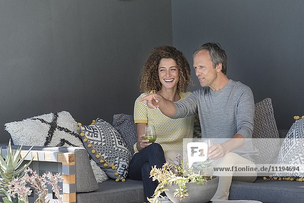 Ein glückliches Paar sitzt auf einer Couch und hält Gläser mit Gemüsesaft.