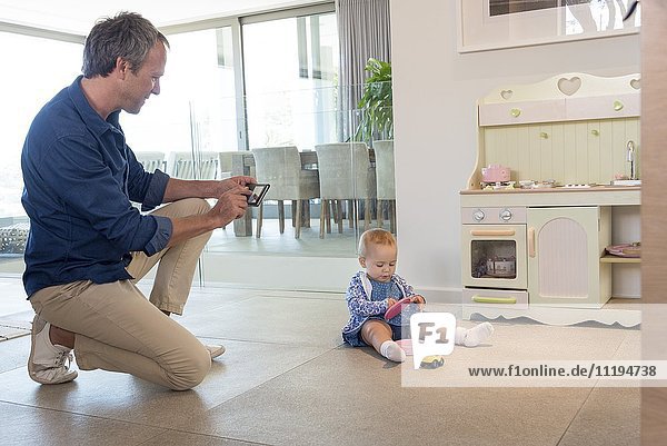 Mature man taking picture of her baby daughter playing with toys