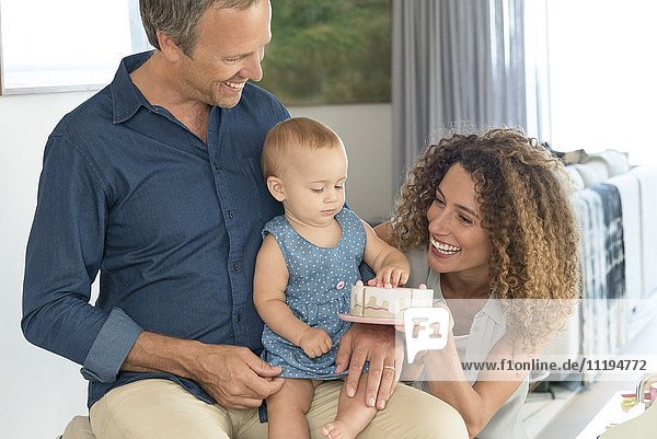 Happy woman giving toy to her baby daughter sitting on her father lap