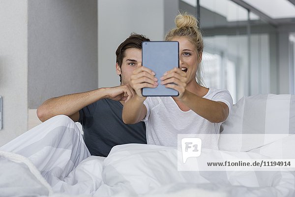 Ein junges Paar  das einen Selfie auf dem Bett nimmt.