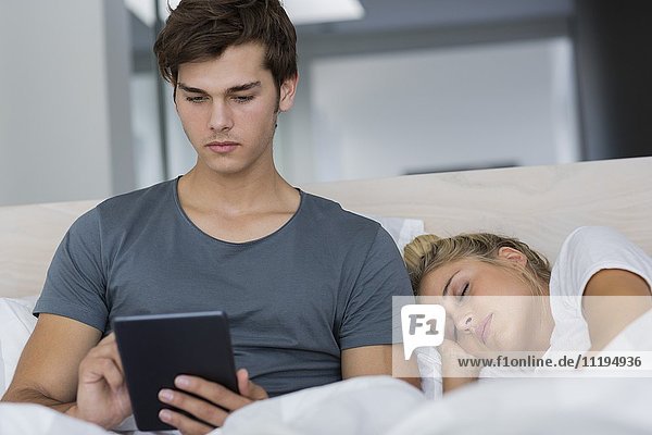 Man using a digital tablet with his girlfriend sleeping near him