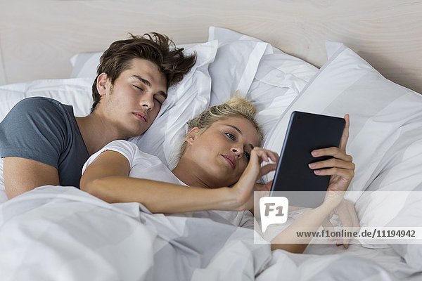 Junge Frau  die ein digitales Tablett benutzt  während ihr Freund in ihrer Nähe schläft.