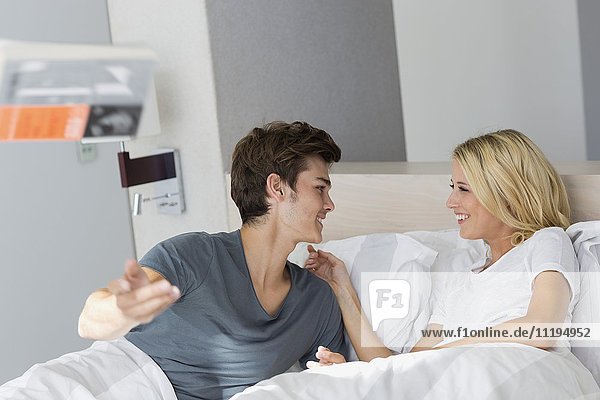 Junges Paar lächelt sich auf dem Bett an.