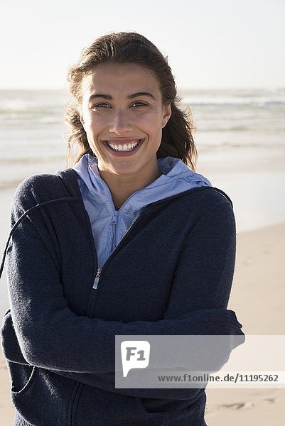 Hübsche junge Frau am Strand stehend und lächelnd