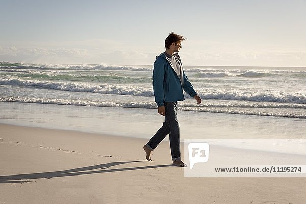 Ein glücklicher junger Mann  der am Strand spazieren geht.