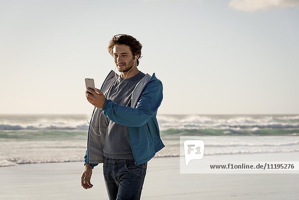 Glücklicher junger Mann mit einem Telefon am Strand
