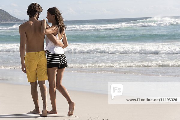 Rückansicht eines jungen Paares beim Spaziergang am Strand