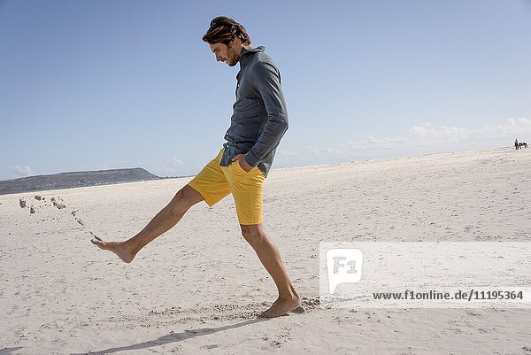 Fröhlicher junger Mann tritt Sand am Strand