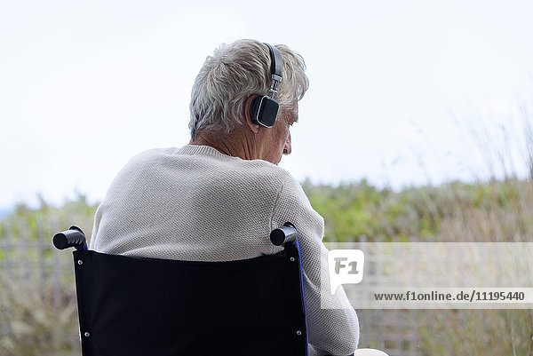 Älterer Mann im Rollstuhl  der Musik über Kopfhörer im Freien hört.