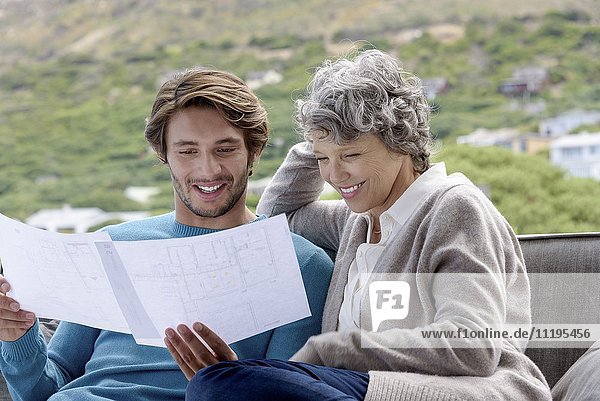 Happy mother with her adult son reading a blueprint outdoors