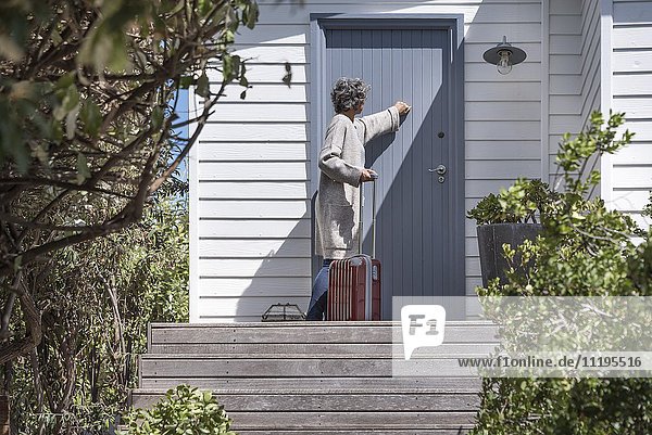 Woman with suitcase knocking on door