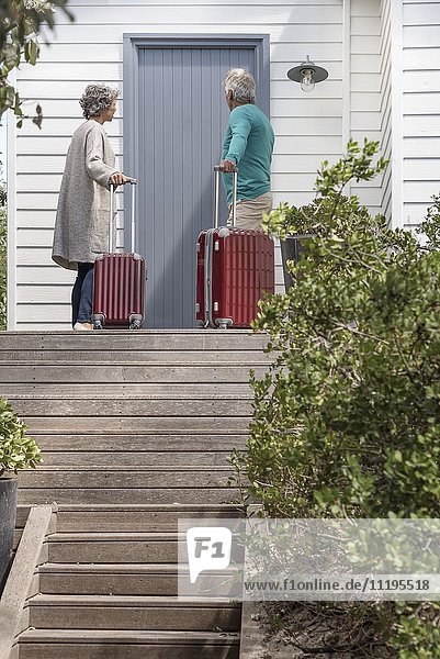 Senior couple with suitcase waiting at front door