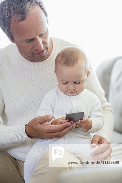 Glücklicher Vater und seine kleine Tochter beim Spielen mit dem Handy auf der Couch