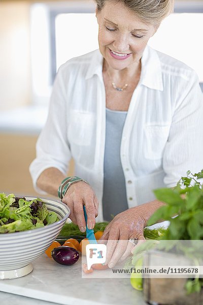 Glückliche Seniorin beim Schneiden von Gemüse in der Küche