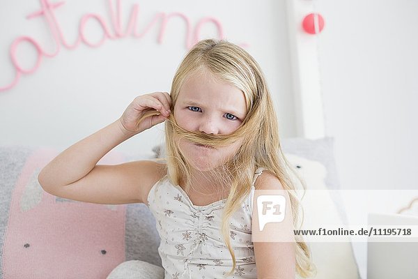Porträt eines kleinen Mädchens  das mit seinen Haaren Schnurrbart macht.