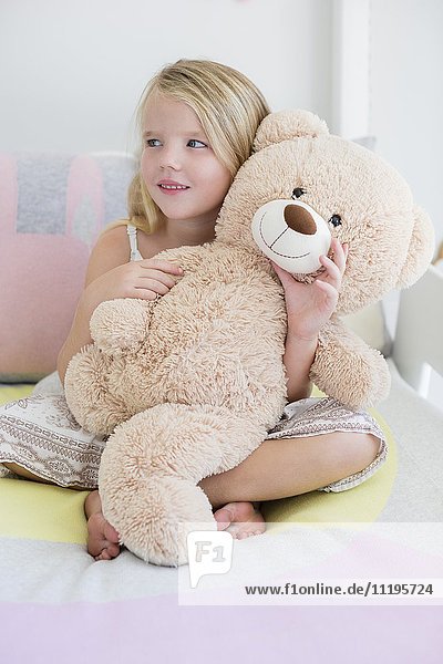 Glückliches kleines Mädchen mit Teddybär im Bett