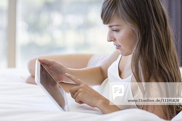 Schöne junge Frau auf dem Bett liegend mit einem digitalen Tablett