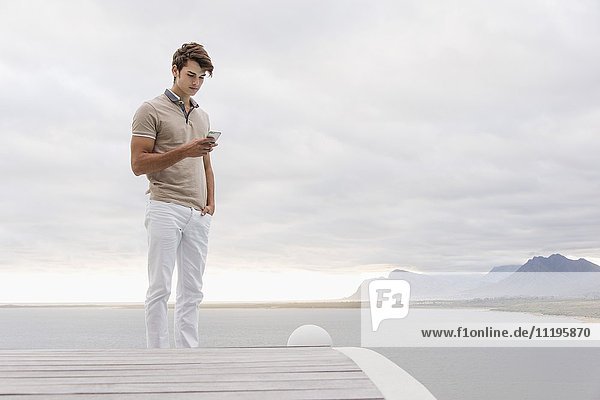 Junger Mann mit einem Smartphone am Seeufer