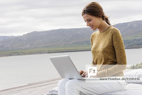 Hübsche junge Frau mit Laptop am Seeufer