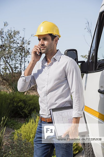 Männlicher Ingenieur im Gespräch auf einem Handy per Van vor Ort