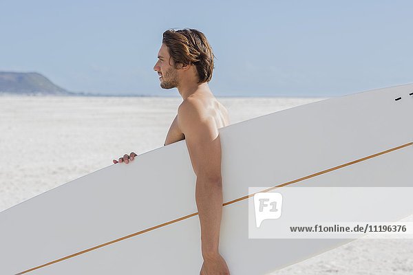 Seitenprofil eines Mannes mit Surfbrett am Strand