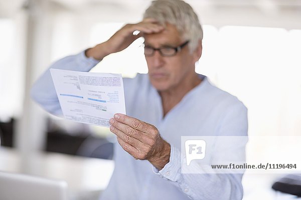 Besorgter älterer Mann beim Lesen eines Briefes auf dem Tisch
