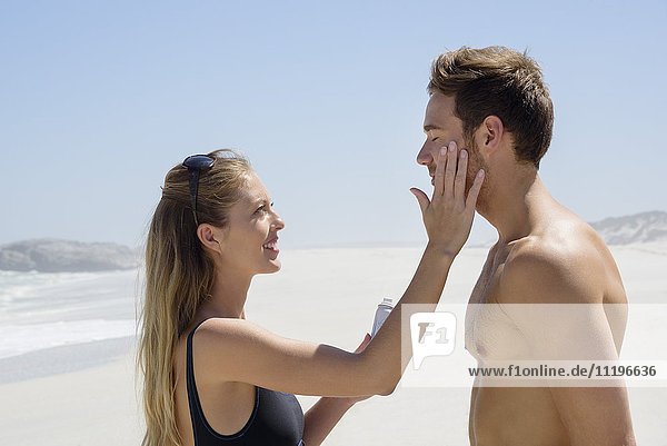 Frau  die Sonnencreme auf das Gesicht ihres Mannes aufträgt.