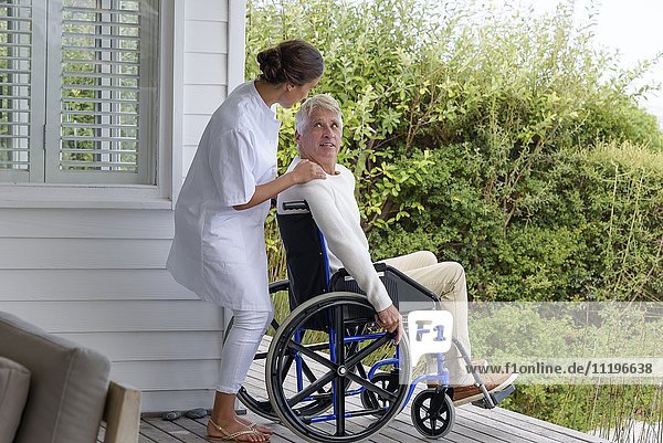 Krankenschwester als Assistentin eines älteren Mannes im Rollstuhl auf der Veranda
