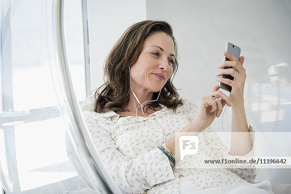 Reife Frau beim Musikhören mit Smartphone im Sessel