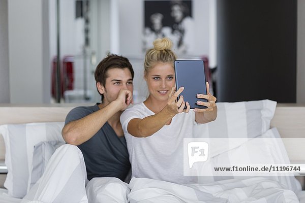 Ein junges Paar  das einen Selfie auf dem Bett nimmt.