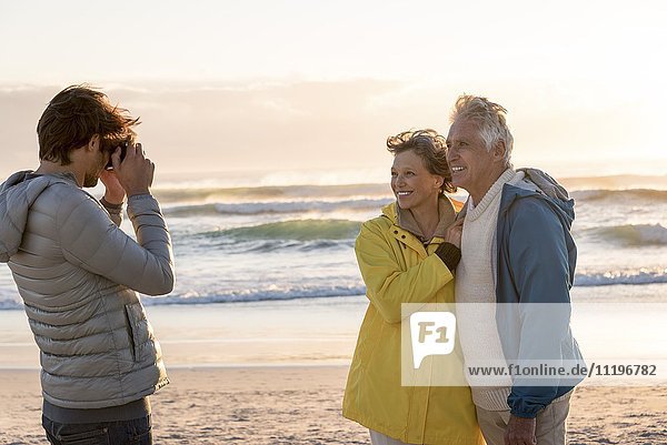Young man taking a picture of his parents with camera on the beach