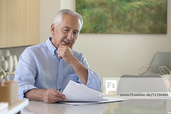 Älterer Mann  der den Papierkram zu Hause erledigt.